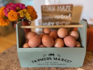 Farmers market brown eggs in rustic wooden crate with colorful fall flowers.